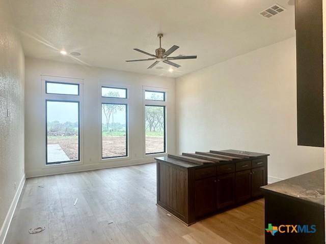 unfurnished office with visible vents, light wood-style flooring, a ceiling fan, and a healthy amount of sunlight