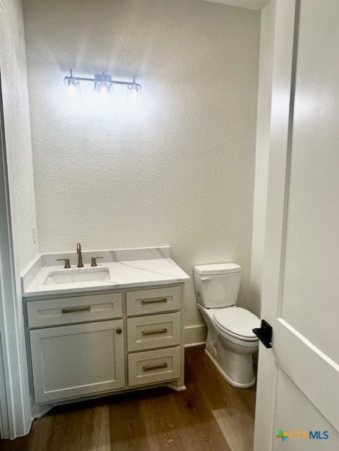 half bath featuring toilet, wood finished floors, vanity, and a textured wall