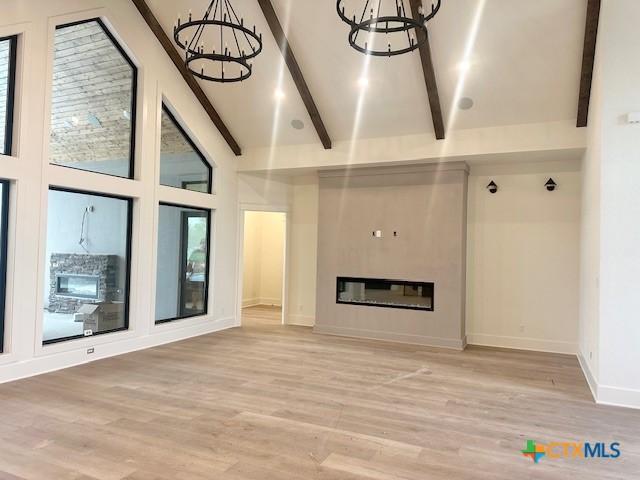 unfurnished living room with beamed ceiling, an inviting chandelier, and light wood-style floors