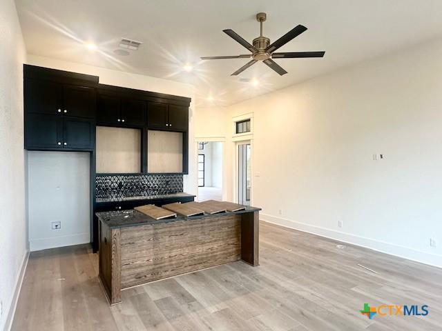 kitchen featuring backsplash, ceiling fan, light wood-type flooring, and dark cabinetry