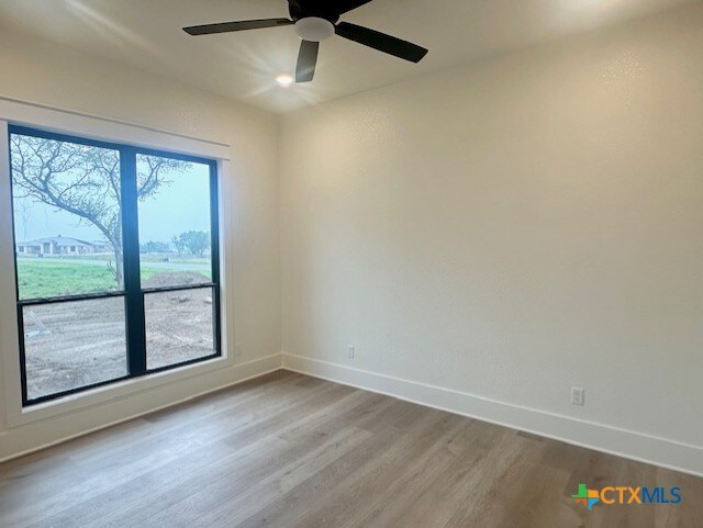 unfurnished room with wood finished floors, baseboards, and a ceiling fan