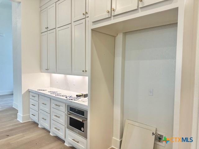 kitchen featuring baseboards, light wood-type flooring, light countertops, white cabinetry, and oven