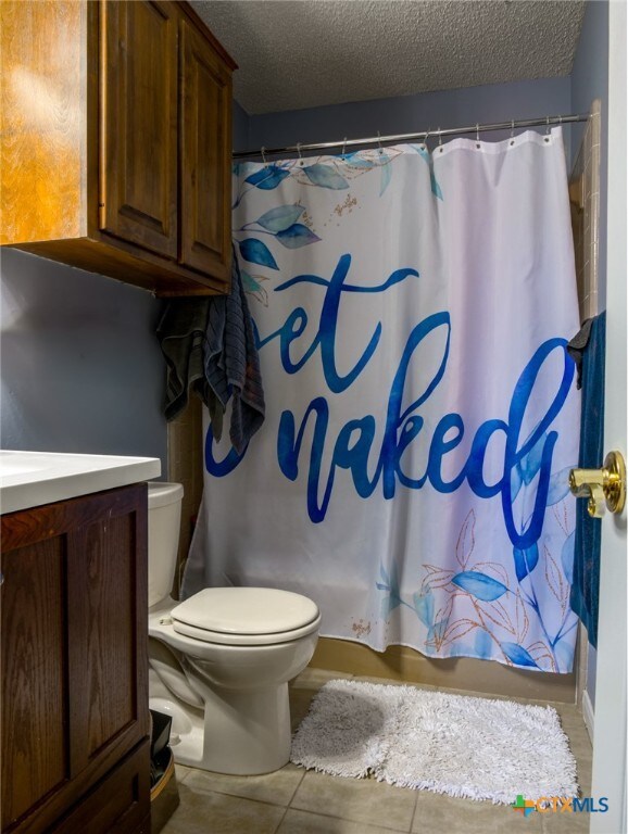 full bathroom with tile patterned floors, vanity, a textured ceiling, and toilet