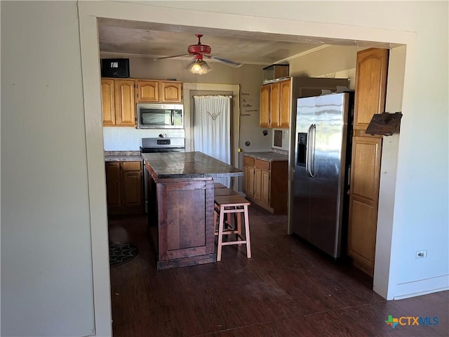 kitchen featuring stainless steel appliances, ceiling fan, dark wood-type flooring, a center island, and a breakfast bar area