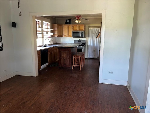 kitchen featuring appliances with stainless steel finishes, dark wood finished floors, brown cabinets, and a breakfast bar area