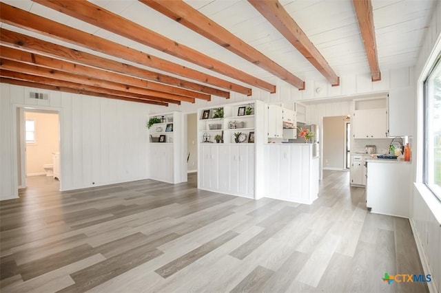 unfurnished living room featuring a sink, light wood-style flooring, visible vents, and beamed ceiling