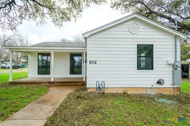 exterior space with covered porch, roof with shingles, and a lawn