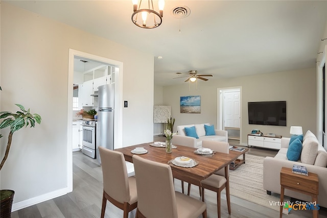 dining space featuring ceiling fan with notable chandelier, visible vents, baseboards, and wood finished floors