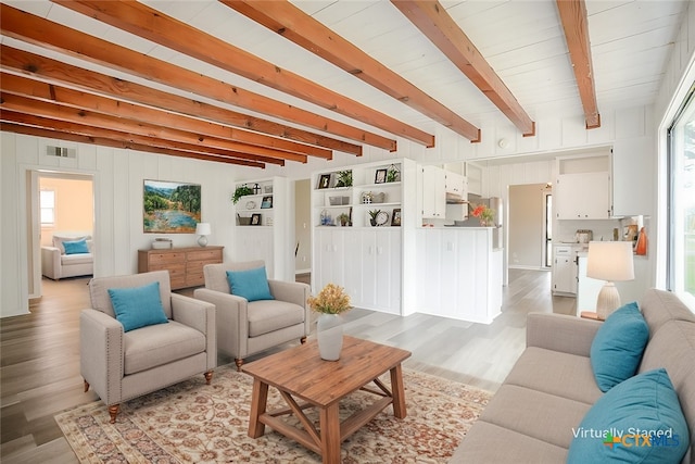 living area with light wood-style floors, a wealth of natural light, visible vents, and beamed ceiling