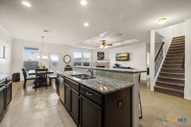 kitchen with dishwasher, sink, an island with sink, pendant lighting, and dark stone countertops