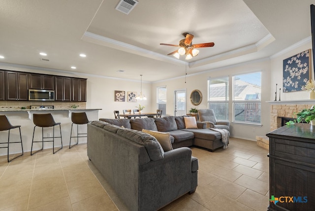 tiled living room featuring a stone fireplace, crown molding, ceiling fan, and a raised ceiling