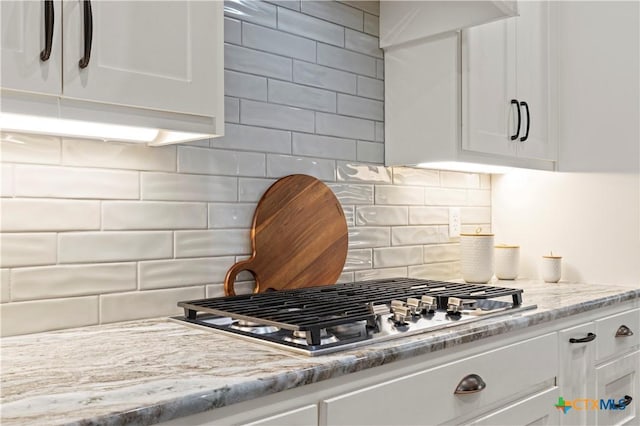 kitchen featuring white cabinets, light stone countertops, stainless steel gas stovetop, and decorative backsplash