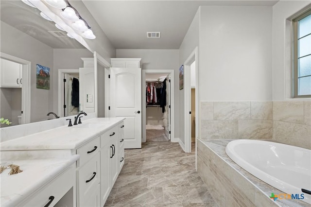 bathroom with tiled tub, plenty of natural light, and vanity