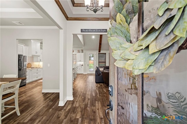 hallway with a raised ceiling, an inviting chandelier, ornamental molding, and dark wood-type flooring