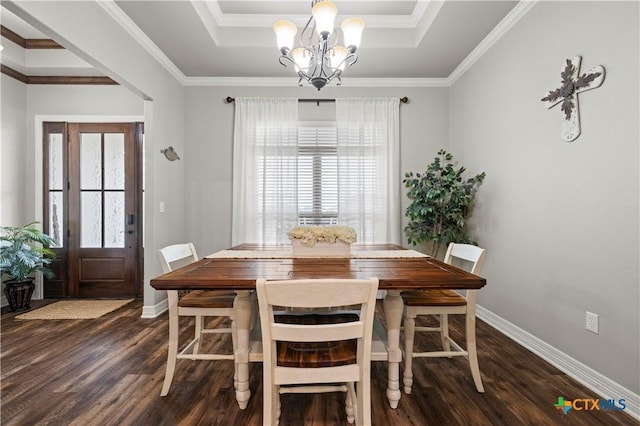 dining area with ornamental molding, dark wood-type flooring, an inviting chandelier, and a tray ceiling