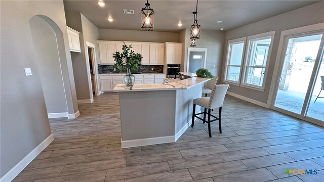 kitchen with tasteful backsplash, a breakfast bar area, hanging light fixtures, a kitchen island with sink, and white cabinets