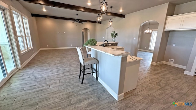 kitchen featuring light wood-type flooring, beam ceiling, decorative light fixtures, and white cabinets