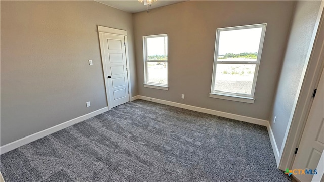 empty room with plenty of natural light, ceiling fan, and dark carpet