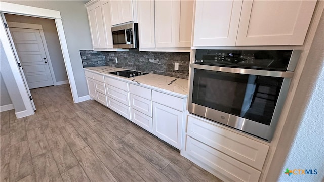 kitchen featuring stainless steel appliances, light stone countertops, white cabinets, light wood-type flooring, and decorative backsplash