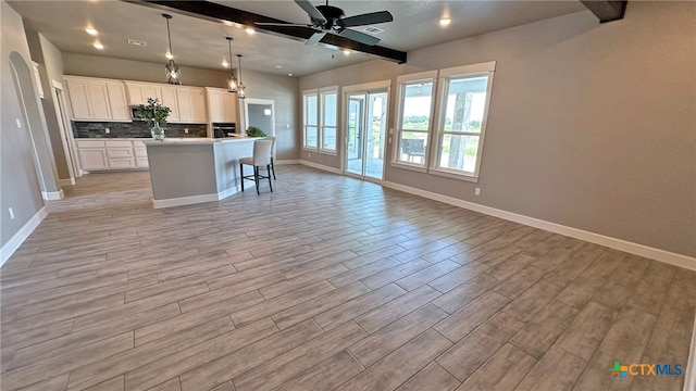 kitchen featuring light wood-type flooring, a center island with sink, white cabinetry, and decorative light fixtures