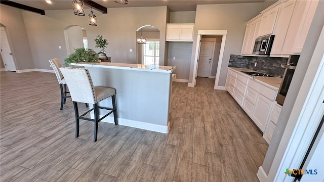 kitchen featuring a center island with sink, light wood-type flooring, appliances with stainless steel finishes, beam ceiling, and white cabinets