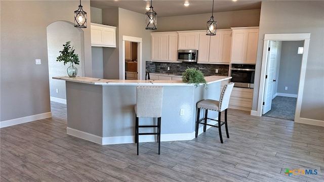 kitchen with a kitchen bar, stainless steel appliances, tasteful backsplash, white cabinetry, and decorative light fixtures