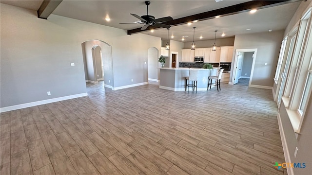 unfurnished living room with ceiling fan, beam ceiling, and light wood-type flooring