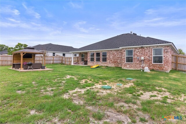 rear view of house featuring a lawn, brick siding, a gazebo, and a fenced backyard