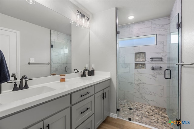full bathroom with double vanity, a shower stall, a sink, and wood finished floors