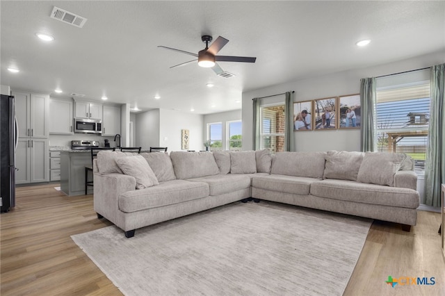 living area featuring ceiling fan, light wood-style flooring, and visible vents