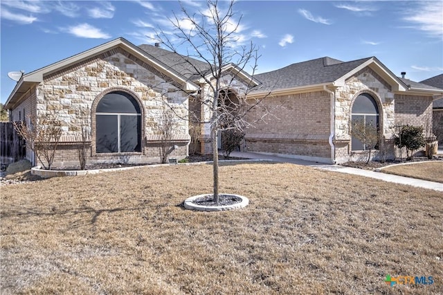 view of front of home with a front yard, stone siding, brick siding, and roof with shingles