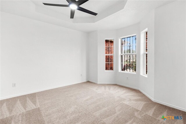 empty room with a tray ceiling, ceiling fan, carpet floors, and baseboards