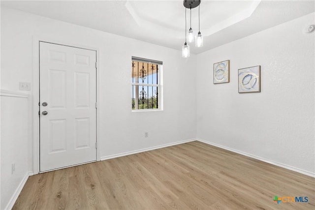 empty room featuring baseboards, a raised ceiling, and light wood-style flooring