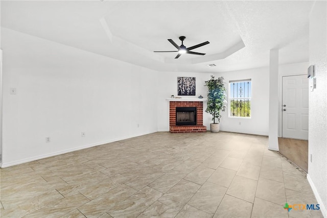 unfurnished living room with a ceiling fan, a tray ceiling, baseboards, and a brick fireplace