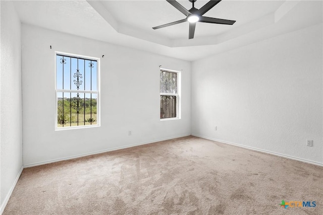 empty room featuring a raised ceiling, ceiling fan, carpet, and baseboards