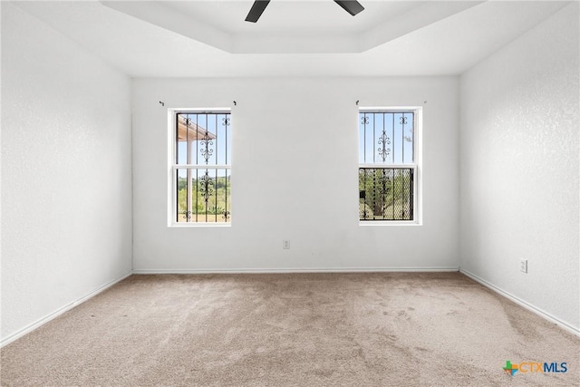 carpeted empty room with ceiling fan, a tray ceiling, and baseboards