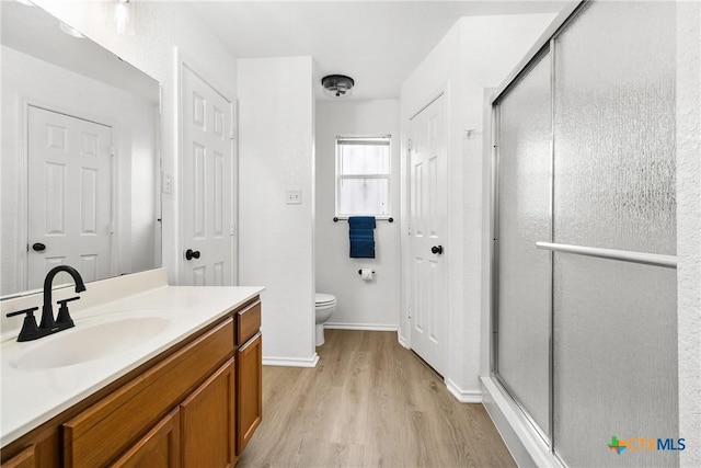 full bath featuring toilet, vanity, a shower stall, and wood finished floors