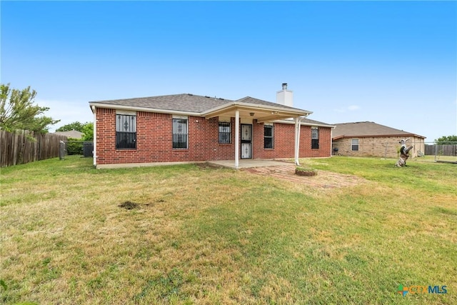 view of front of home with a patio, a front lawn, a chimney, brick siding, and fence