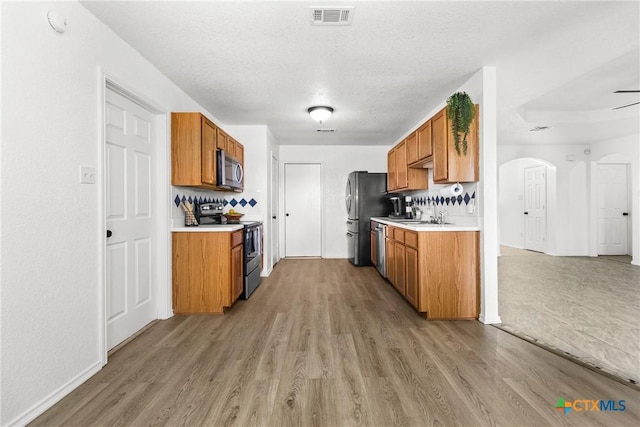 kitchen featuring brown cabinets, visible vents, stainless steel appliances, light countertops, and light wood-type flooring