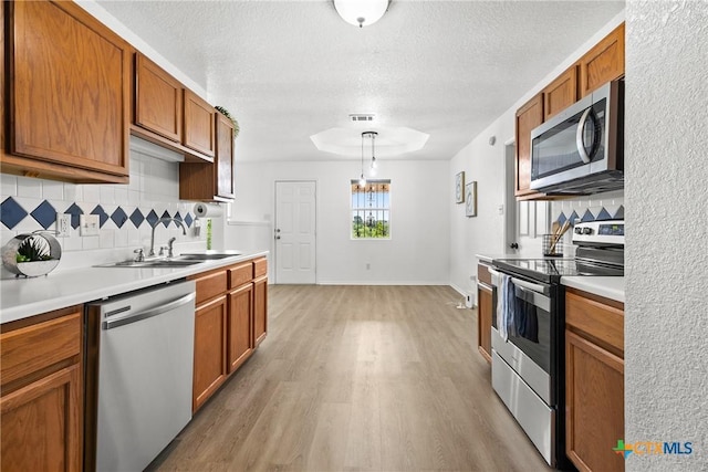 kitchen featuring decorative backsplash, brown cabinetry, stainless steel appliances, a sink, and light wood-type flooring