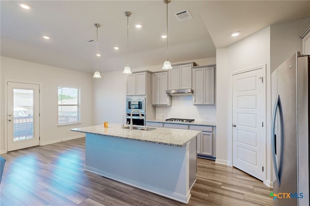 10259 Juniper Oaks, Boerne, TX 78006 - kitchen with appliances with stainless steel finishes, wood finished floors, light stone counters, a kitchen island with sink, and decorative light fixtures