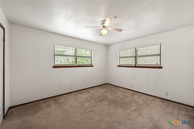 carpeted empty room featuring a textured ceiling, a ceiling fan, and baseboards