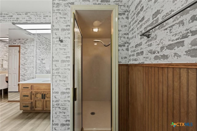 bathroom with a stall shower, wainscoting, vanity, and wood finished floors