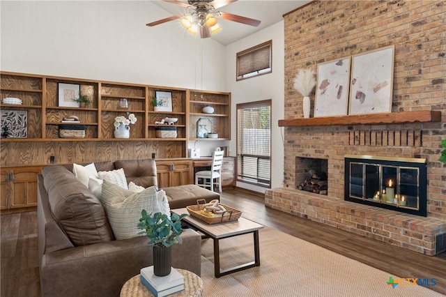 living area with ceiling fan, high vaulted ceiling, a brick fireplace, and wood finished floors