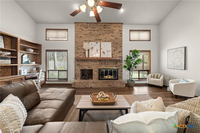 living room with ceiling fan, a high ceiling, a brick fireplace, and wood finished floors