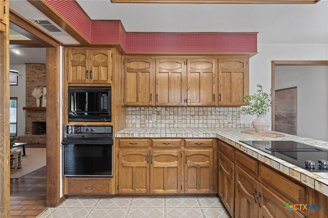 kitchen with tasteful backsplash, visible vents, brown cabinetry, tile countertops, and black appliances