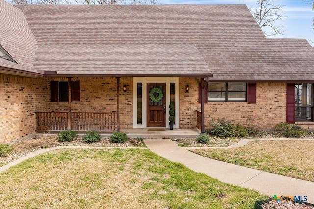 view of front of home featuring a shingled roof, a front yard, brick siding, and a porch