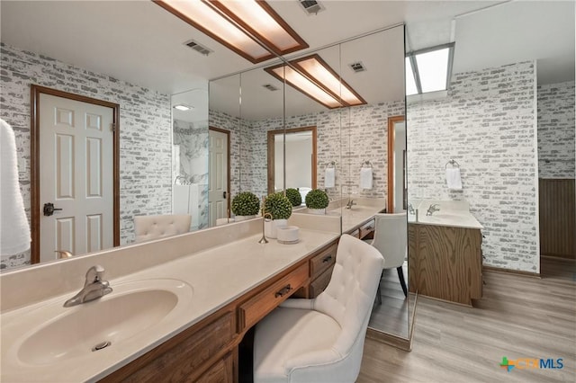 bathroom with visible vents, two vanities, a sink, and wood finished floors