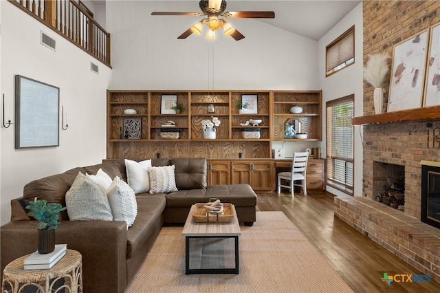 living room with a ceiling fan, a brick fireplace, visible vents, and light wood-style floors