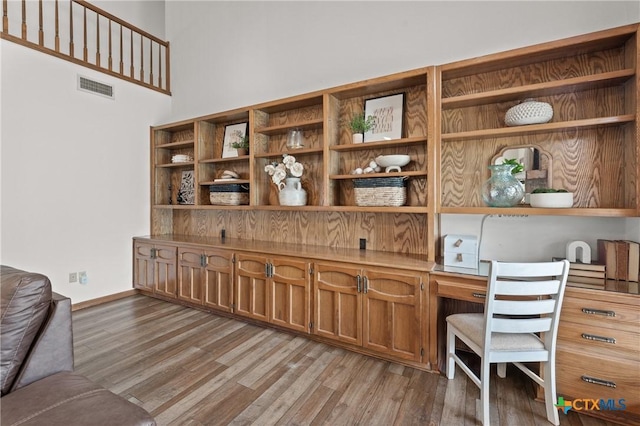 office area with baseboards, light wood-style flooring, visible vents, and built in desk